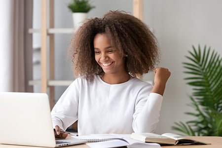 student looking at laptop smiling and raising a triumphant fist