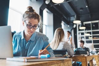 Female student writing while using laptop