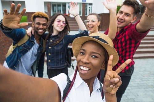 grupo de estudiantes de secundaria que se toman una selfie frente a su escuela