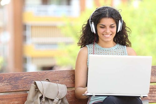 mujer con auriculares sentada en el banco usando una computadora portátil