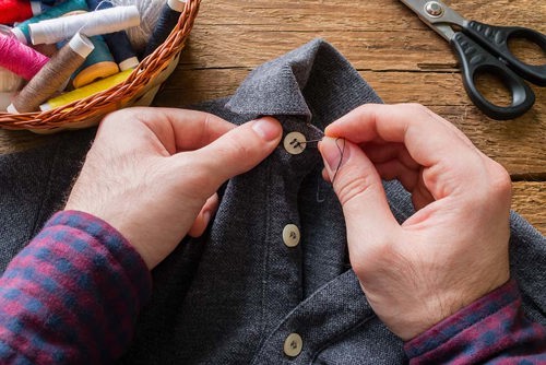 persona cosiendo un botón en una camisa